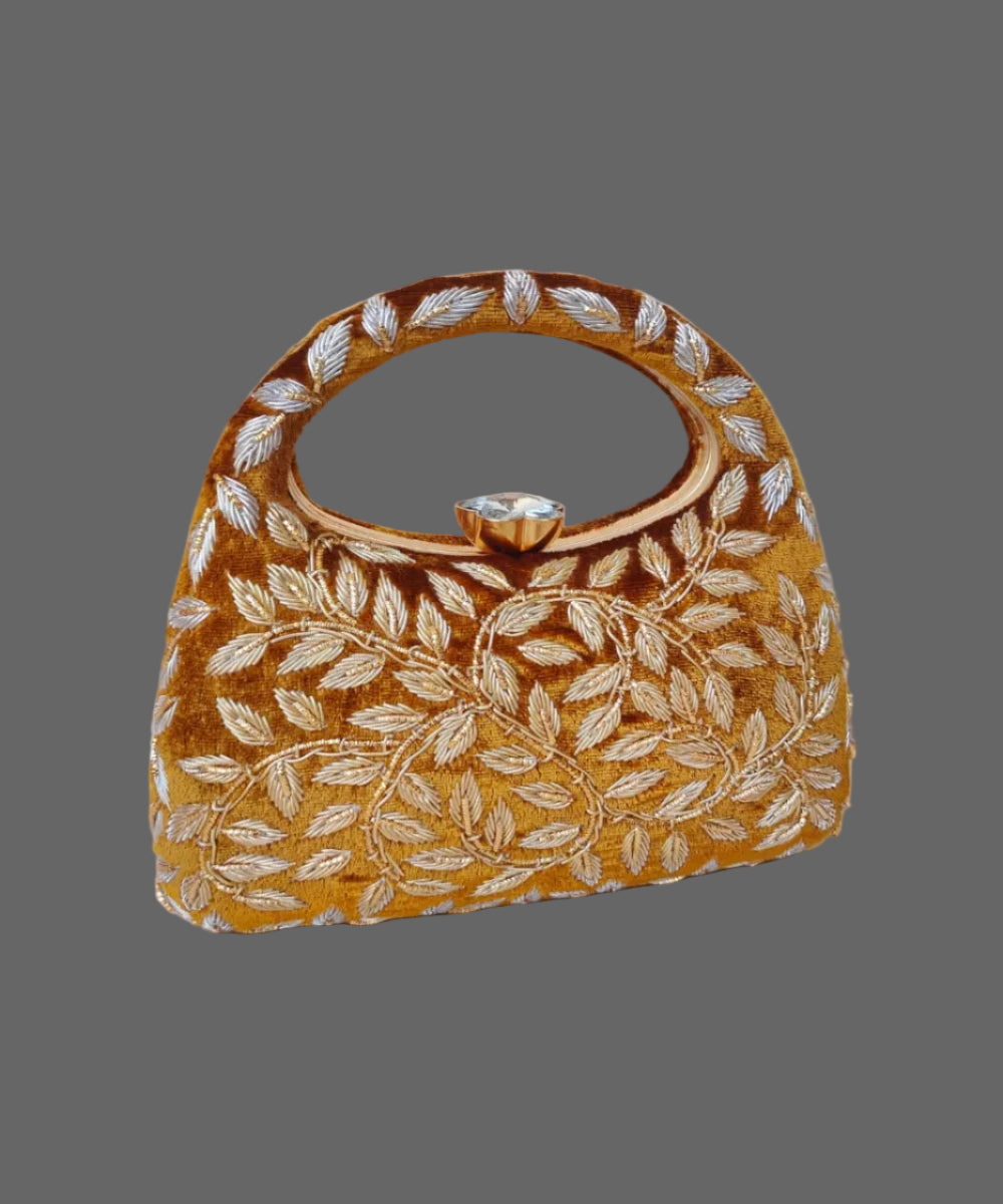 Gold handbag with leaf pattern on a wooden surface with a vase of flowers in the background