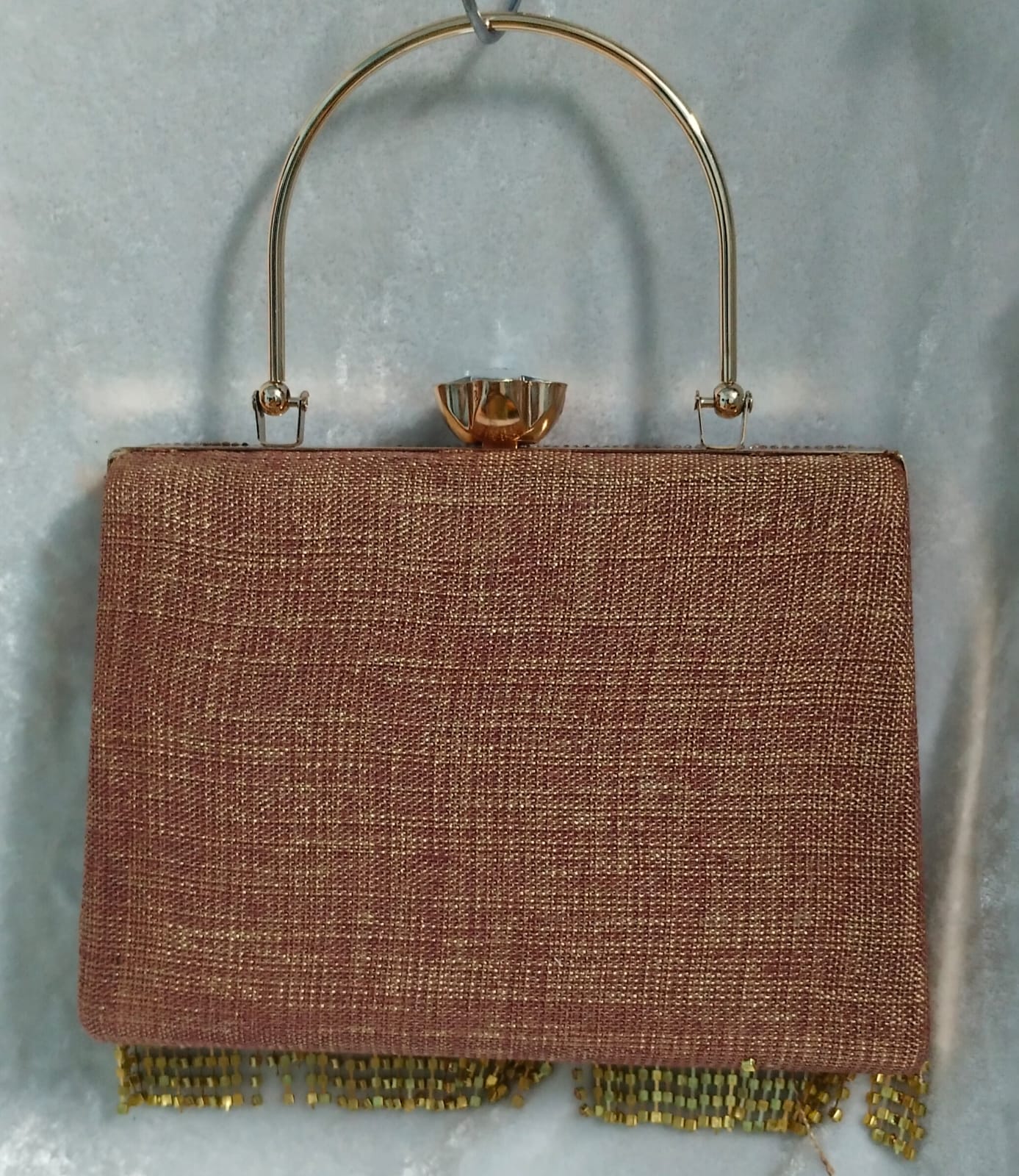 Brown textured handbag with gold handle and fringe on a light gray background