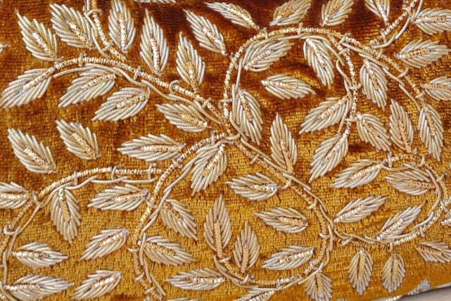 Gold handbag with leaf pattern on a wooden surface with a vase of flowers in the background