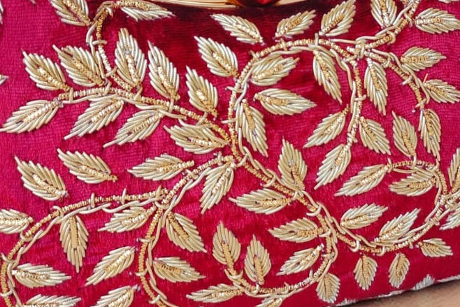 fuchsia handbag with gold leaf patterns on a wooden surface