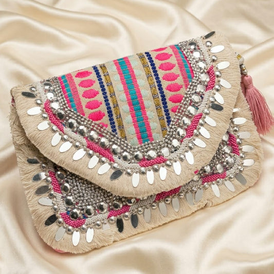 A beige bohemian clutch bag decorated with colorful pink, blue, and yellow stripes, silver mirror work, and pink tassels, resting on a cream satin fabric background.