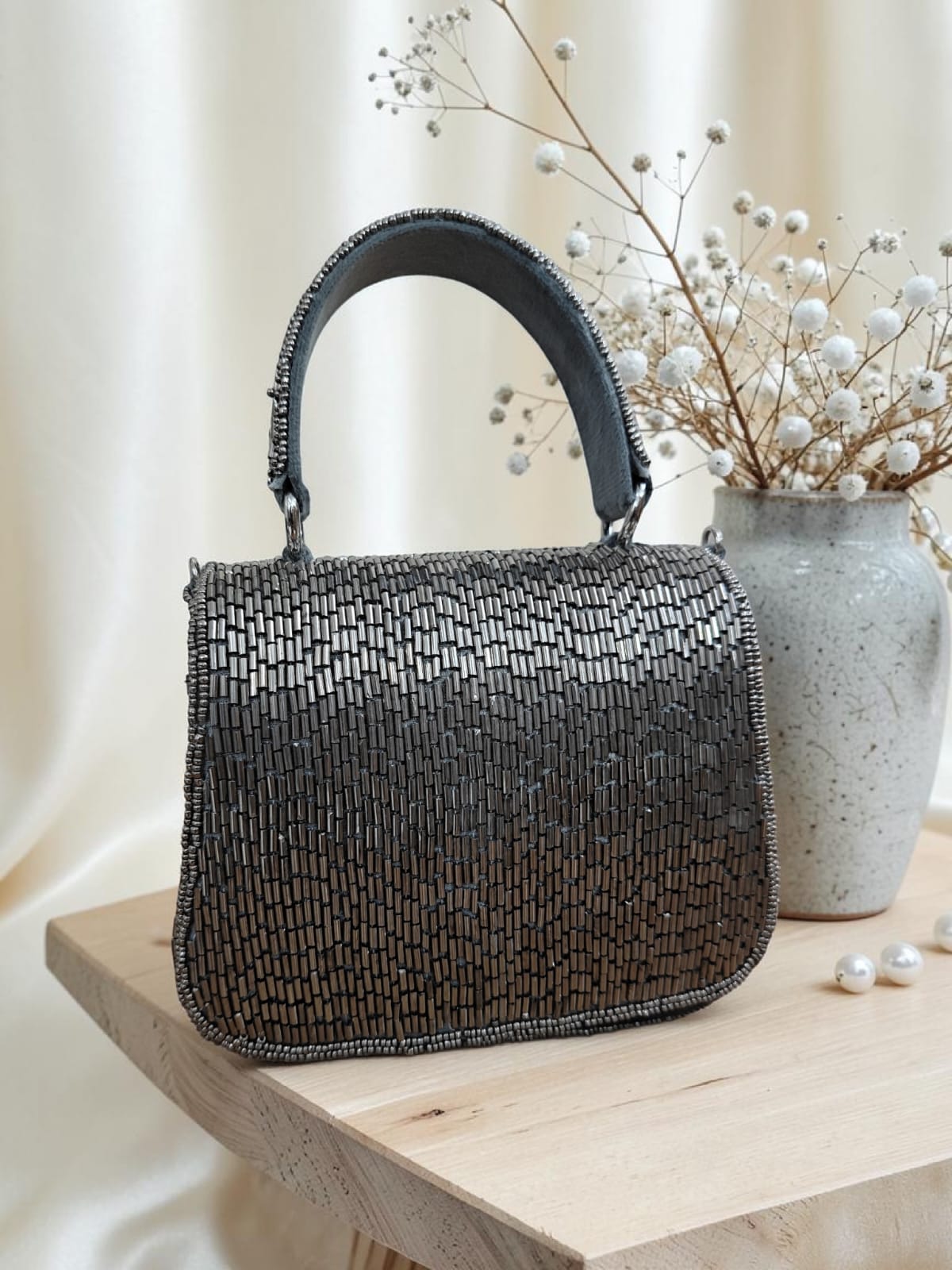 Beaded handbag on a wooden surface with a vase and flowers in the background