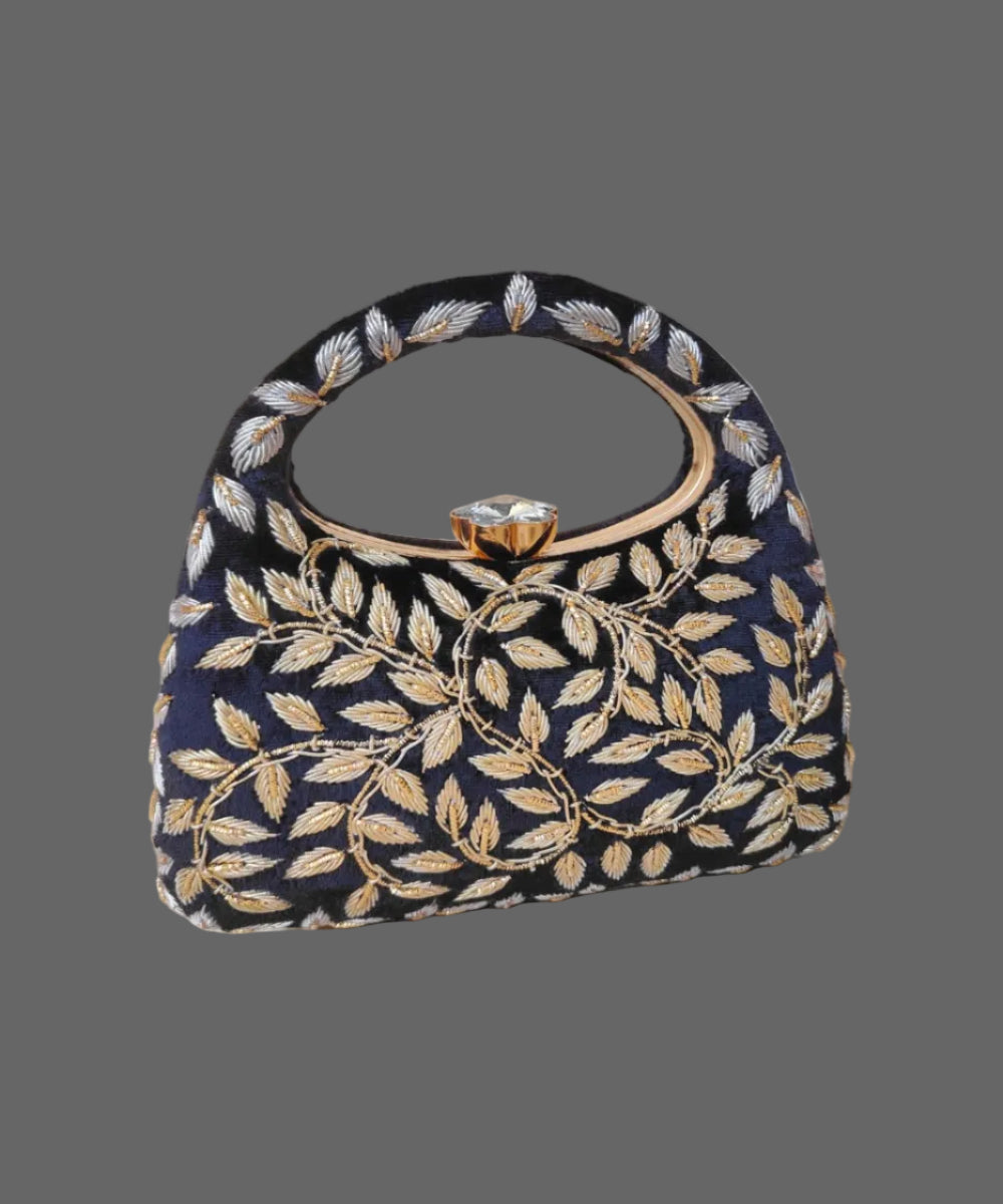 Navy blue handbag with gold leaf patterns on a wooden surface with a vase of flowers in the background.