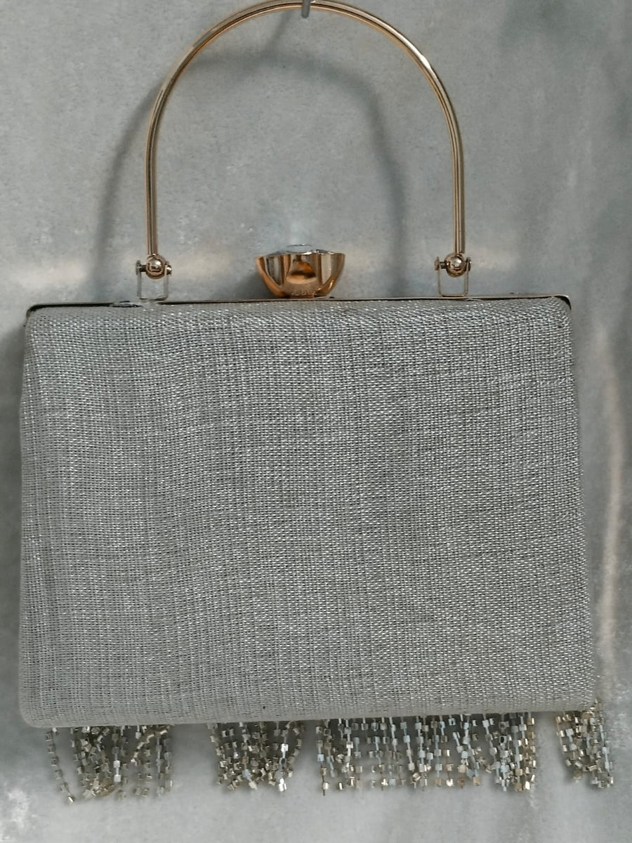 Gray handbag with a gold handle and silver fringe on a gray background